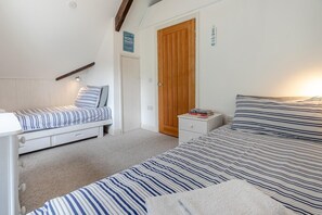 A bedroom with two beds, a wooden door, and a small bedside table with books. - 2 Bed in Fowey (oc-p00839) (Fowey)