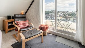 A modern living room with a leather chair, a small wooden side table, and a view of a cityscape through large windows. - 2 Bed in Fowey (oc-p00839) (Fowey)