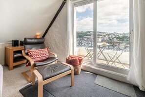 A modern living room with a leather chair, a small wooden side table, and a view of a cityscape through large windows. - 2 Bed in Fowey (oc-p00839) (Fowey)
