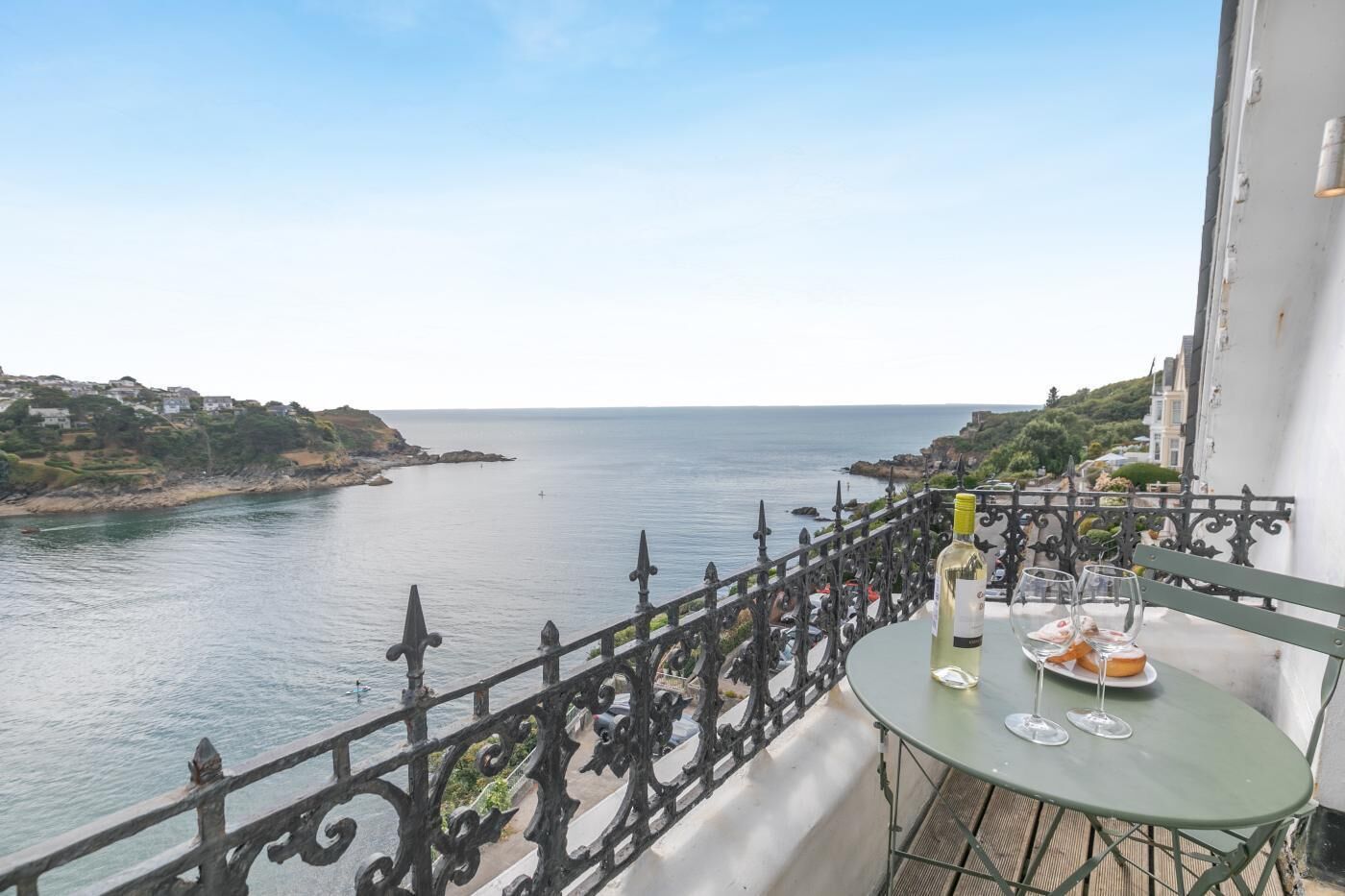 En balkon med havudsigt, et bord med flaske og glas, samt et gelænder.