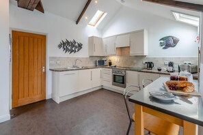 A modern kitchen with white cabinets, a microwave, a stove, and a breakfast setup on the counter. - 2 Bed in Fowey (oc-p00839) (Fowey)