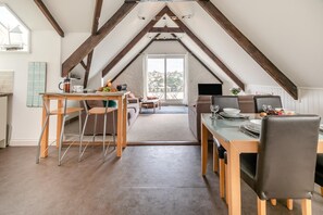Um quarto no sótão com teto inclinado, uma sala de jantar com mesa e cadeiras, e vista através de uma grande janela.