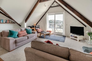 A loft-style living room with a sofa, armchair, and a TV on a stand. - 2 Bed in Fowey (oc-p00839) (Fowey)