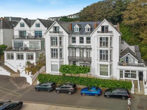 A multi-story residential building with a central balcony, a staircase, and a parking area with several cars. - 2 Bed in Fowey (oc-p00839) (Fowey)
