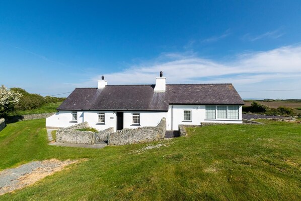A white house with a dark roof, stone walls, and a grassy yard. - 3 Bed in Y Fali (oc-bow70) (Valley)