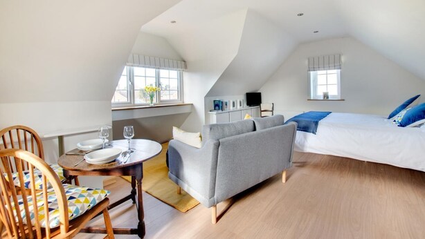 A loft-style bedroom with a bed, sofa, dining table, and a small kitchenette.