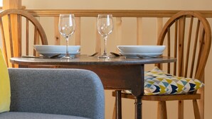 A dining table with two wine glasses and plates, a wooden chair with a patterned cushion, and a grey sofa.