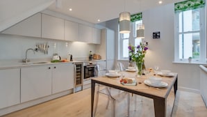 A modern kitchen with white cabinets, a wooden dining table, and pendant lights. - 2 Bed in Fowey (oc-p00703) (Fowey)