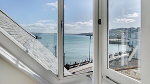 Blick aus einem Fenster auf ein ruhiges Meer mit klarem Himmel, eine Anlegestelle und eine entfernte Küstenlinie mit Gebäuden.