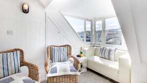 Ein gemütliches Zimmer mit schrägen Wänden, weißen Wänden und Blick auf die Stadt durch große Fenster.