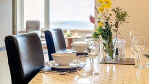 A dining table set with plates, bowls, and wine glasses, with a vase of flowers and a view of the outdoors. - 2 Bed in St Ives (oc-gmn19) (Carbis Bay)