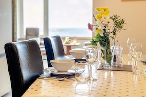 Ein Esstisch ist mit Tellern, Schüsseln und Weingläsern gedeckt, dazu steht eine Blumenvase und man hat Blick ins Freie.