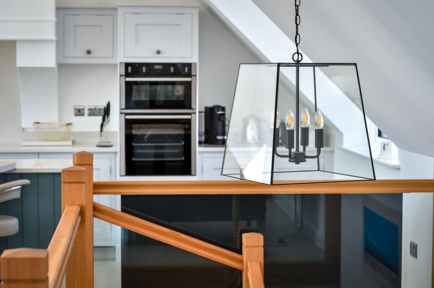 A modern kitchen with white cabinets, a built-in oven, and a hanging pendant light with four bulbs.