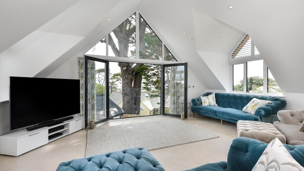 Ein modernes Wohnzimmer mit einem großen Flachbildfernseher, einem blauen Sofa und einer Glastür, die auf einen Balkon führt.