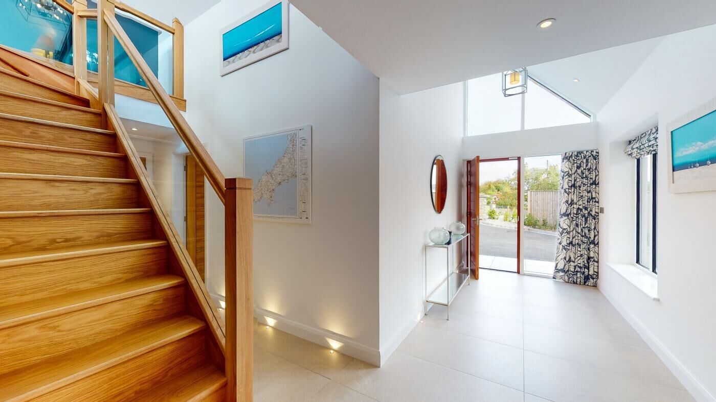 Un pasillo amplio con una escalera de madera, un ventanal grande y una puerta que da al exterior.