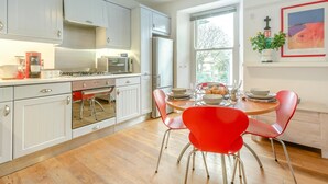 Une cuisine moderne avec des meubles blancs, un réfrigérateur en acier inoxydable et un coin repas agrémenté de chaises rouges et d’une table en bois.
