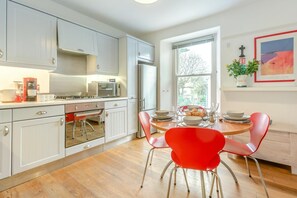 A modern kitchen with white cabinets, a stainless steel refrigerator, and a dining area with red chairs and a wooden table. - 2 Bed in St Ives (oc-sunpol) (Saint Ives)