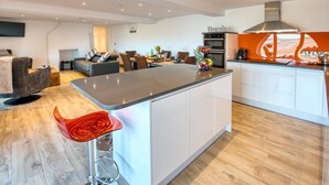 Cozinha moderna com ilha central, área de refeições com sofá e cadeiras, e sala de estar com televisão.