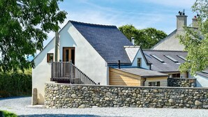Ein modernes Haus mit einer Steinwand, einem geneigten Dach und einer Holztreppe, die zu einem Balkon führt.