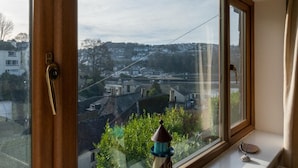 Una habitación con un ventanal grande que da a un paisaje urbano, una mesita con un objeto decorativo y una puerta con pomo dorado.