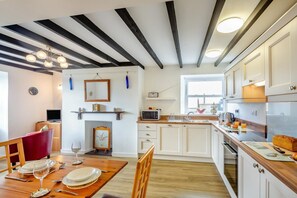 A modern kitchen with white cabinets, a wooden dining table set for four, and a built-in oven. - 3 Bed in Aberdaron (oc-wag407) (Aberdaron)