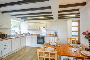 A modern kitchen with white cabinets, a wooden dining table, and a built-in oven. - 3 Bed in Aberdaron (oc-wag407) (Aberdaron)