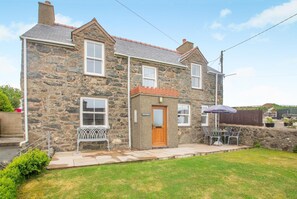 A stone house with a front door, a small porch, and a patio area with outdoor furniture. - 3 Bed in Aberdaron (oc-wag407) (Aberdaron)