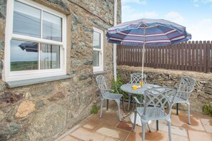 A stone building with a window, a patio table with chairs, and a striped umbrella. - 3 Bed in Aberdaron (oc-wag407) (Aberdaron)