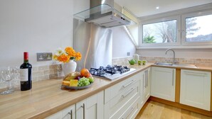 A modern kitchen with a gas stove, a glass range hood, and a window with a view of trees.