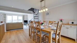 A spacious dining area with wooden chairs and a table set for four, a kitchen with white cabinets, and a staircase leading to an upper level.