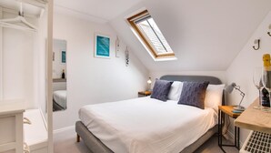 Un dormitorio con tragaluz, una cama con ropa de cama blanca, una mesita de noche con lámpara y un pequeño calentador.