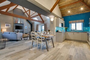 Ein großzügiges Loft mit freiliegenden Holzbalken, einem Essbereich, einer Küche und einem Wohnzimmer mit Sofa und Fernseher.