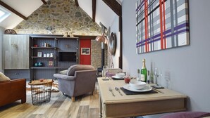 Una sala de estar acogedora con techo de piedra, chimenea, comedor con mesa dispuesta para dos personas y televisor sobre una estantería.