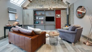 Un salón acogedor con techo de piedra, chimenea, sofá, sillón y lámpara.