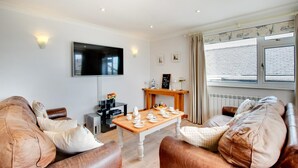 A modern living room with leather sofas, a wooden coffee table, a flat-screen TV, and a dining table set for four. - 3 Bed in Abersoch (oc-kook72) (Abersoch)
