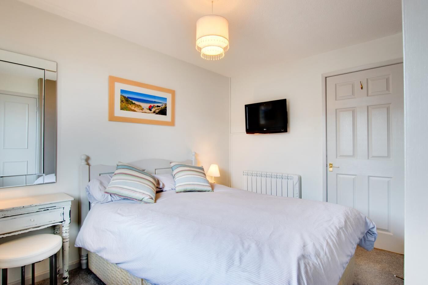 Une chambre à coucher avec un lit, une table de chevet, une lampe et un téléviseur fixé au mur.