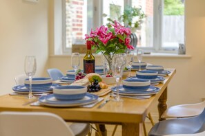 Mesa de jantar posta com pratos azuis e brancos, uma garrafa de vinho e um vaso com flores cor-de-rosa.