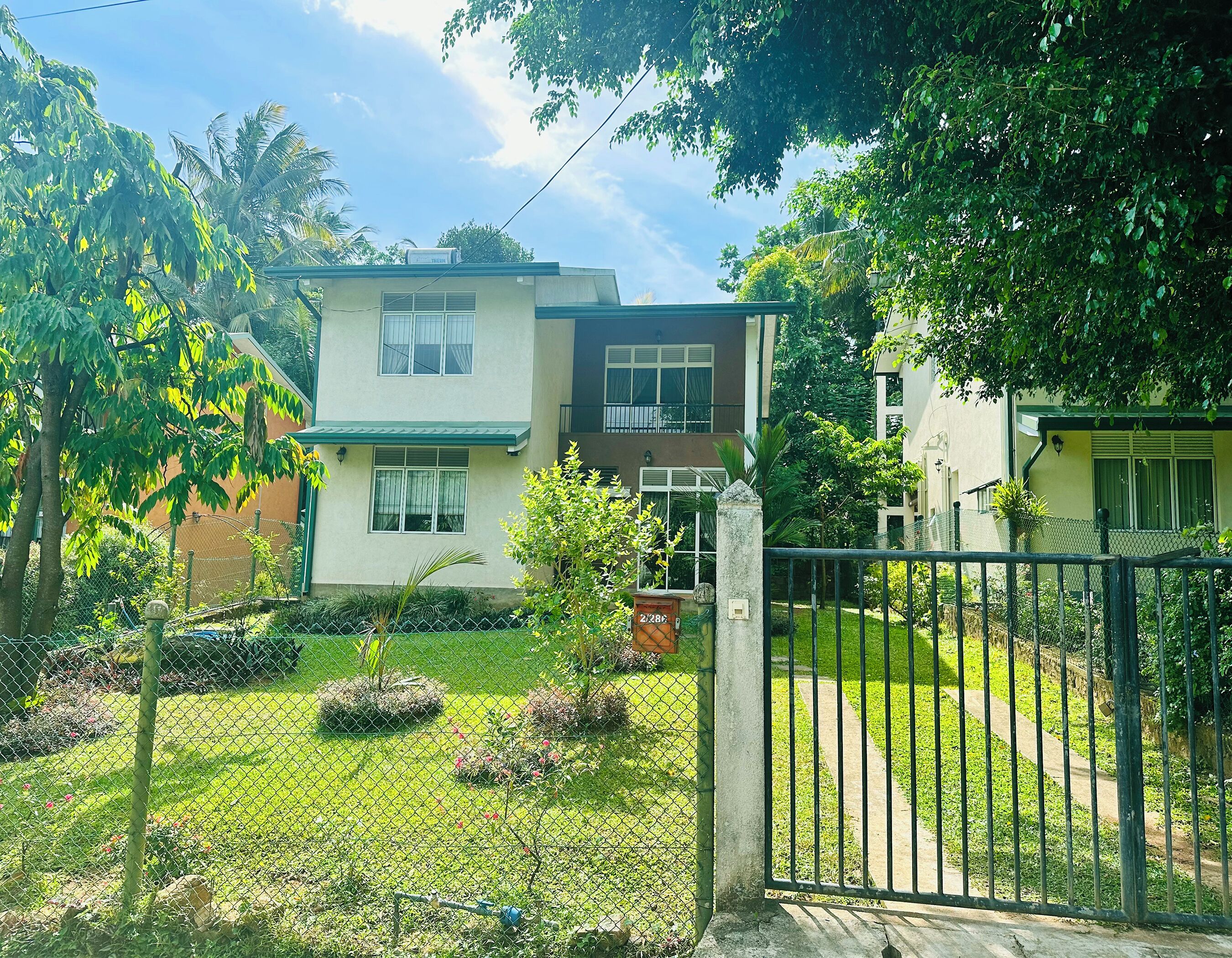 A two-story residential building with a green roof, a fenced yard, and a small garden area.