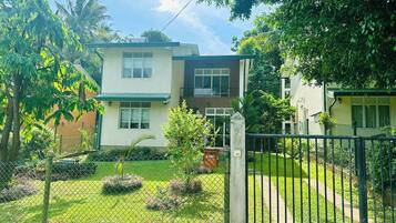 A two-story residential building with a green roof, a fenced yard, and a small garden area.