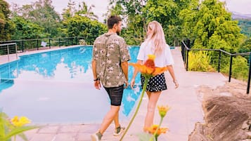 Ein Paar spaziert an einem Pool entlang, mit Blick auf üppiges Grün und Bäume.