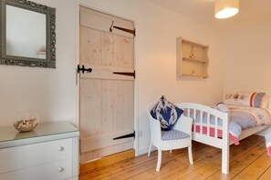Ein Zimmer mit einem weißen Kleiderschrank, einem Bett mit blau-weiß gestreifter Bettdecke, einem weißen Stuhl mit blauem Kissen und einem kleinen Regal mit einer Dekoration.