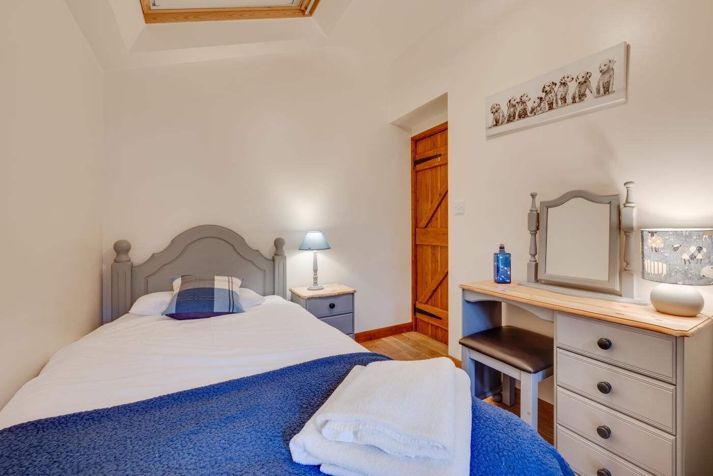 A bedroom with a bed, bedside table, lamp, dresser, and a wooden door.