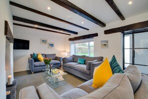 A modern living room with two sofas, a glass coffee table, and a TV mounted on the wall. - 5 Bed in Little Petherick (oc-p00736) (Tregonna)