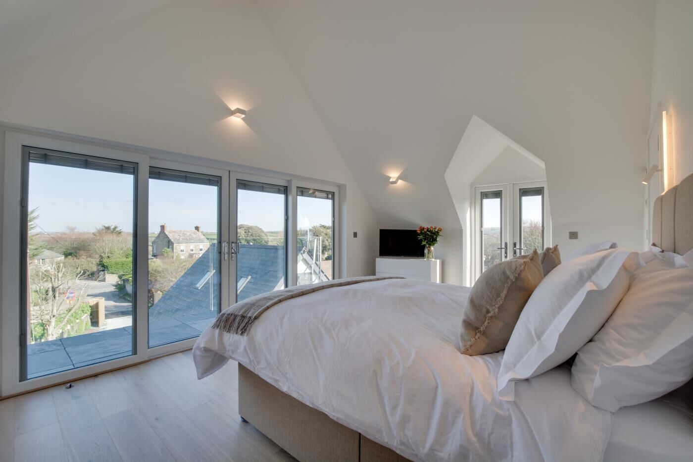 A bedroom with a large bed, multiple windows, and a TV.