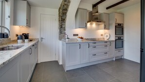 Een moderne keuken met grijze kastjes, een accentmuur van steen en inbouwapparatuur.