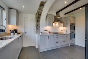 A modern kitchen with grey cabinets, a stone accent wall, and built-in appliances. - 5 Bed in Little Petherick (oc-p00736) (Tregonna)