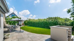 Een terras met een tafel en stoelen, een overdekte zithoek en een verzorgd gazon.