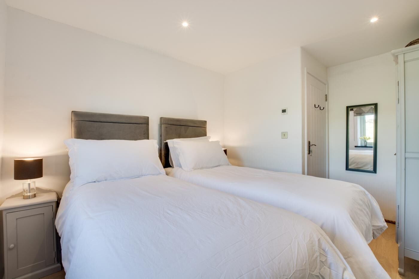 A double bed with a headboard, a bedside table with a lamp, and a door with a mirror.