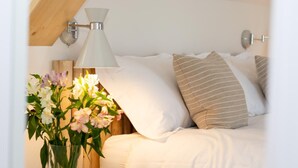 Een net opgemaakt bed met witte lakens, een gestreept kussen en een bloevas op het nachtkastje.