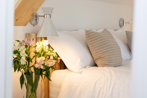 A neatly made bed with white bedding, a striped pillow, and a vase of flowers on the nightstand. - 5 Bed in Little Petherick (oc-p00736) (Tregonna)